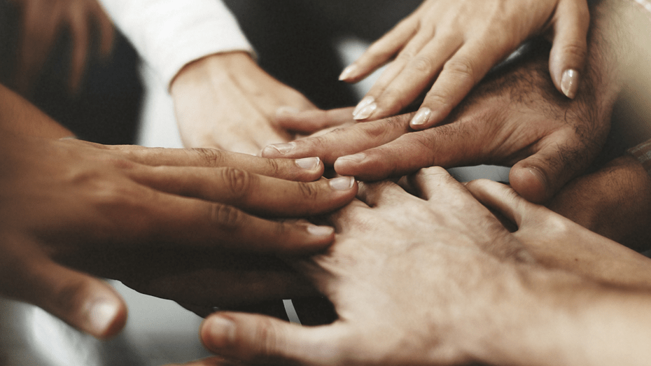 A diverse group of women touch hands in a 